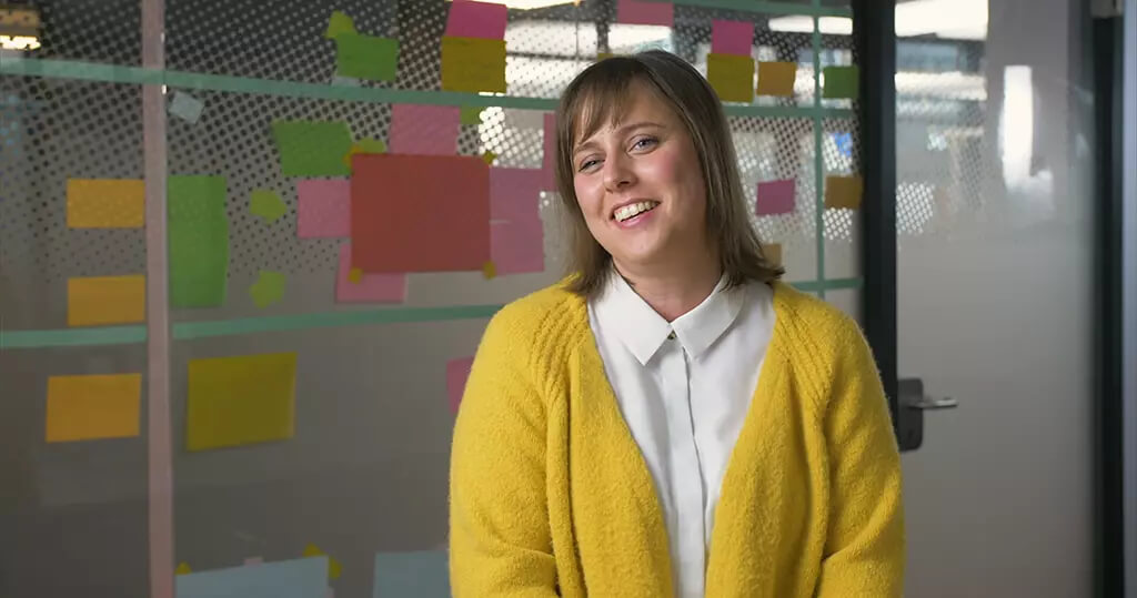 EOS Holding Imagefilm: Frau im gelben Cardigan vor Glaswand mit bunten Post-its